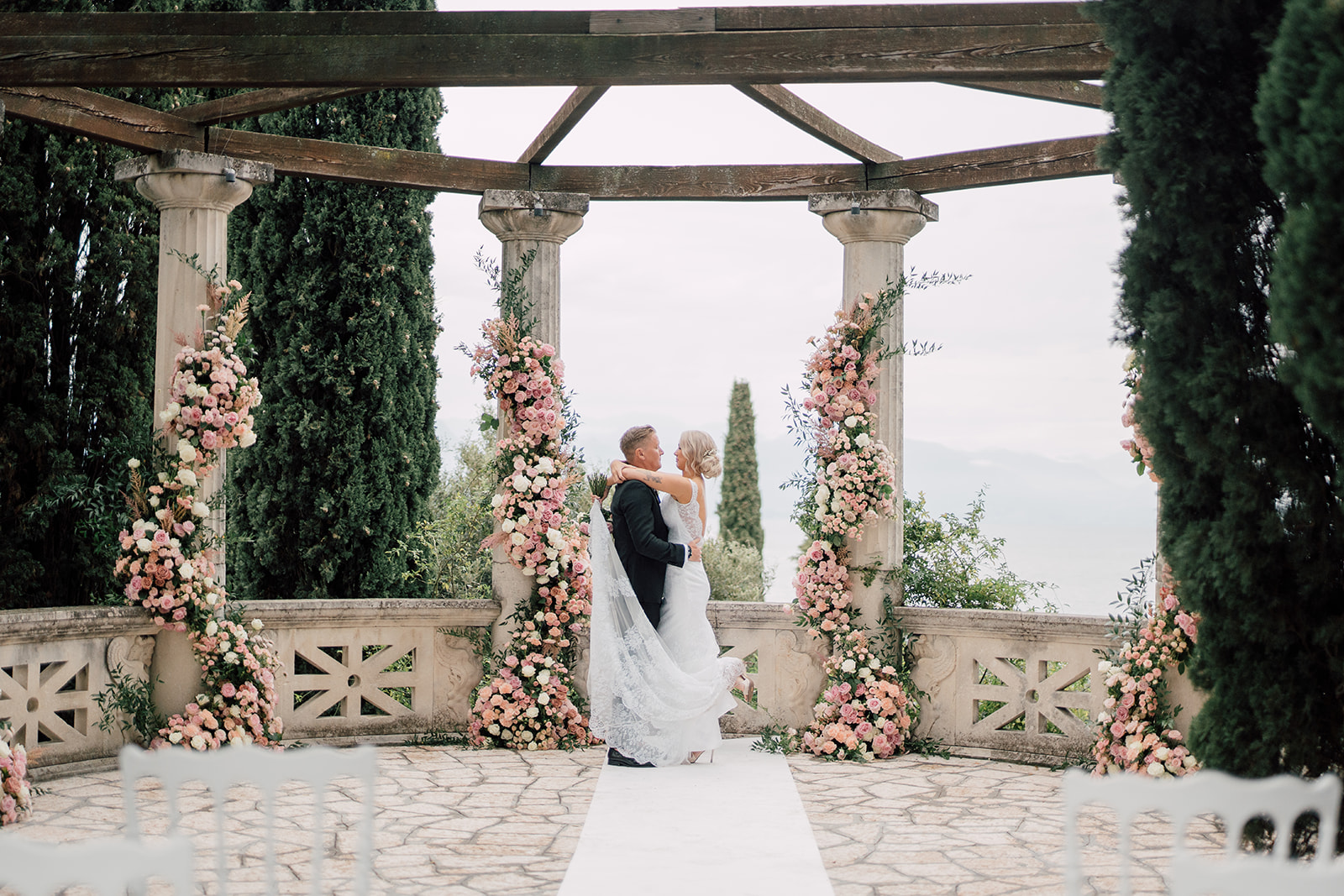 A wedding couple embracing beneath a flower-decorated pergola