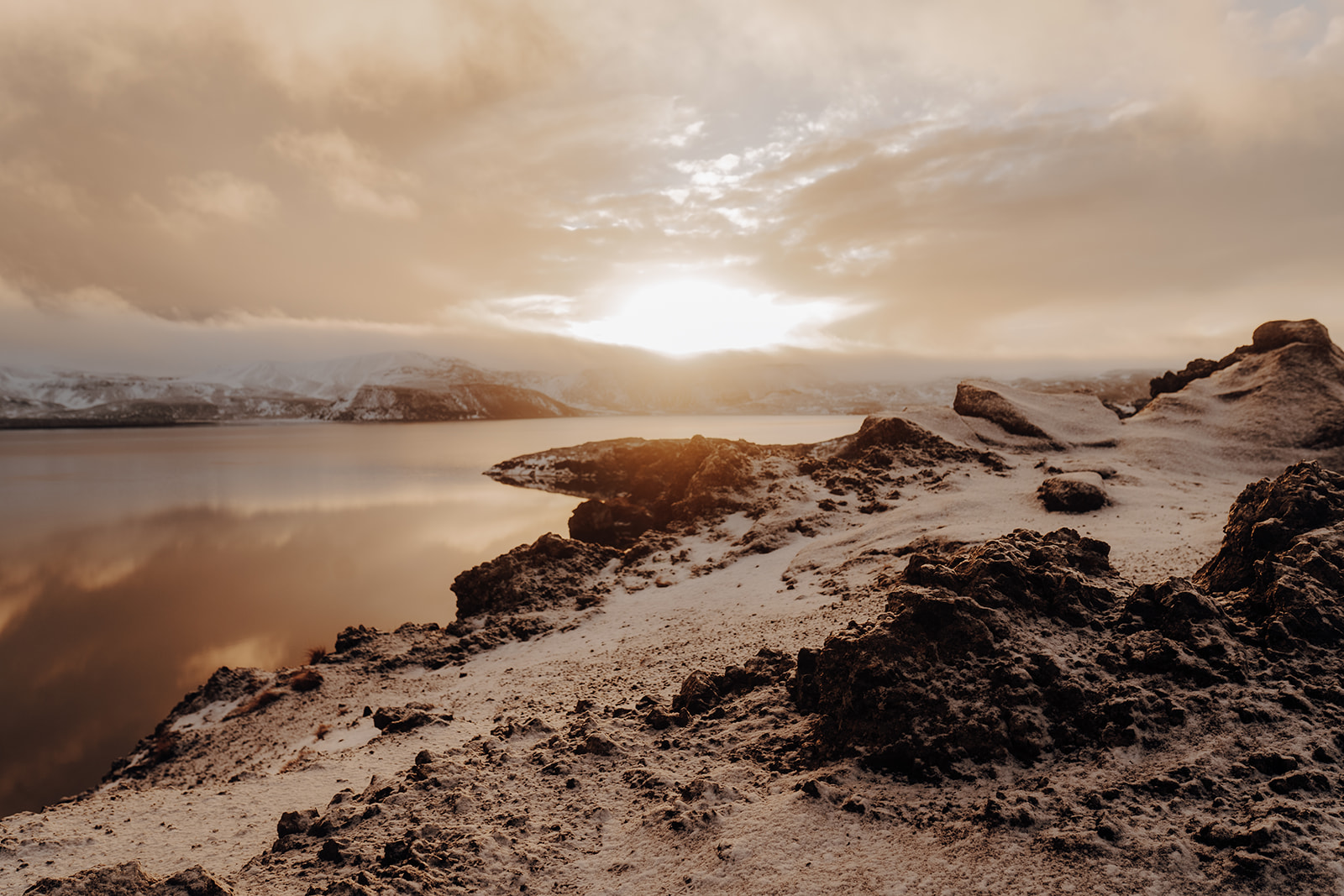 Winter light over an Icelandic lakeshore and snow-dusted lava landscape
